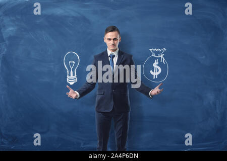 Businessman est titulaire d'une ampoule dans une main et un sac d'argent dans une autre main sur fond bleu ardoise Banque D'Images