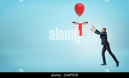 Un petit homme d'essayer d'attraper une grande boîte-cadeau c'est s'envoler sur un ballon. Banque D'Images