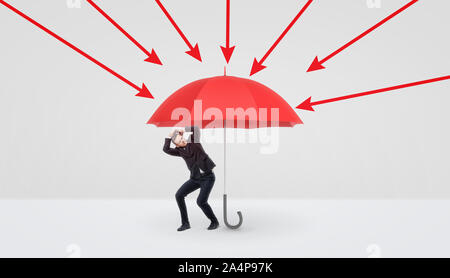 Un petit homme se cachant sous un grand parapluie rouge qui le protège contre les flèches rouges. Banque D'Images