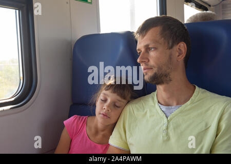 Girl sleeping appuyée sur l'épaule de papa dans un train électrique voiture Banque D'Images