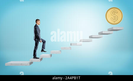 Un homme d'affaires sur fond bleu à monter un escalier en béton où une pièce d'or géant se dresse sur le haut. Banque D'Images