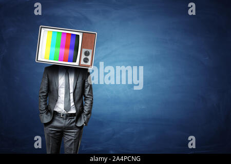 Un homme calme avec les mains dans ses poches porte un vieux téléviseur fort avec barres de couleur sur l'écran. Banque D'Images