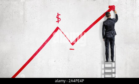 Un homme se tient sur un escabeau et dessine une flèche statistique rouge se déplacer vers le haut avec un signe dollar. Banque D'Images