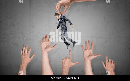 Une main géante est titulaire d'un petit homme d'affaires sur de nombreuses mains saisissant géant sur fond de béton. Banque D'Images