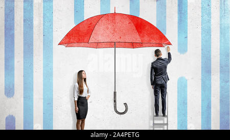 Une femme se tient près d'un mur où un homme d'affaires attire un grand parapluie rouge de les couvrir de la pluie. Banque D'Images