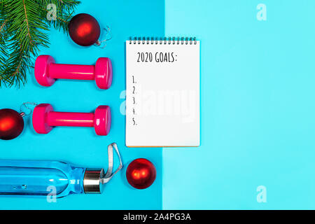 Liste des objectifs pour les vacances du Nouvel An. Sport Noël ensemble avec haltères courtes, bouteille d'eau, des branches de sapin et boules rouges sur le tapis de yoga et bleu sur fond bleu pastel. Mise à plat, vue du dessus, copiez l'espace. Banque D'Images