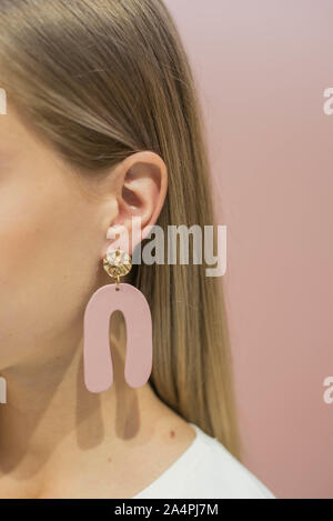 Fait main en plastique sur le boucles d'oreilles de la blonde. Boucles d'oreilles en plastique avec la couleur rose. Banque D'Images