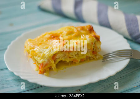 Portion de lasagnes savoureuses sur une assiette blanche sur une table en bois bleu, serviette rayée bleue et blanche. Plats faits maison Banque D'Images
