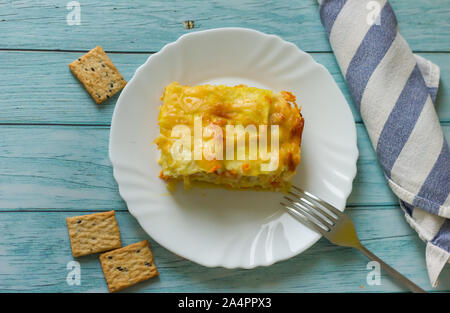 Portion de lasagnes savoureuses sur une assiette blanche sur une table en bois bleu, serviette rayée bleue et blanche. Plats faits maison Banque D'Images