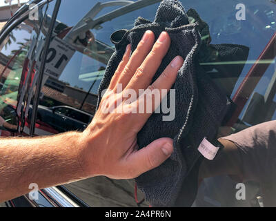 Un homme en voiture de nettoyage avec chiffon en microfibre, concept d'esthétique automobile. Part des employés travailleur utilise sombre propre pour essuyer la voiture après le lavage dans le lave-auto shop Banque D'Images