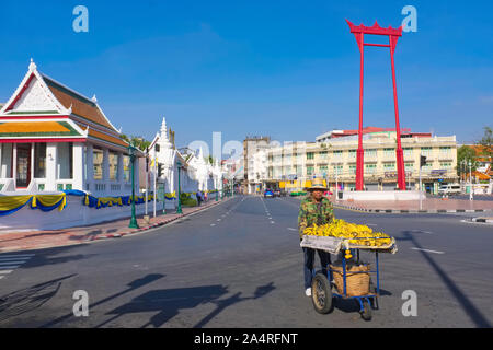 Un vendeur de bananes avec son chariot passe entre Wat Suthat (l) et le site Swing géant (SAO) Ching-Chaa ; Bamrung Muang Rd., Bangkok, Thaïlande Banque D'Images