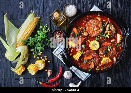 Le pain de viande chevaline, sauce tomate, champignons, légumes et les cors dans une cocotte en céramique noire avec des ingrédients sur une pierre noire sur un sol en bois Banque D'Images