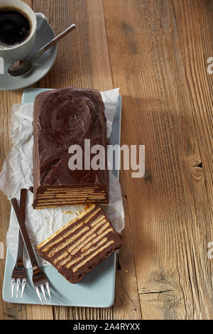 Vue de dessus de tranches de gâteau au chocolat avec des couches de biscuits à l'intérieur, servi sur le bac bleu et tasse de café noir sur table en bois avec copie espace vertical Banque D'Images