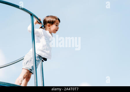 Petite fille jouer sur l'aire de jeux avec ciel bleu Banque D'Images