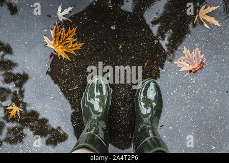 Les pieds dans des bottes en caoutchouc vert olive debout dans une flaque d'eau avec les feuilles tombées. Banque D'Images