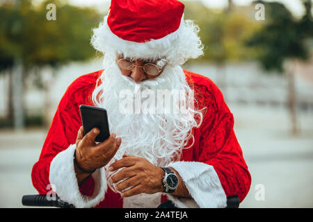 Stock photo de santa claus parlant à un téléphone mobile avec un parc derrière sans organisation. Temps de Noël Banque D'Images