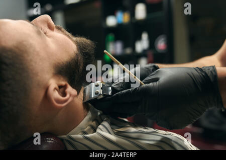 Close up of coiffure s mains porter des gants noirs que faire de nouveau formulaire pour rasoir barbe avec bel homme aux cheveux noirs en coiffure pour homme coiffure.en train de changer son client s hairstyle Banque D'Images