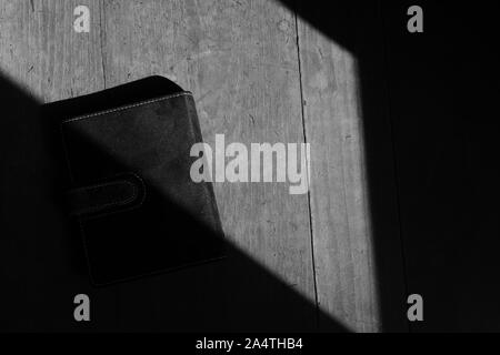 Un livre noir placé sur la surface en bois sous la lumière du soleil, image en noir et blanc Banque D'Images