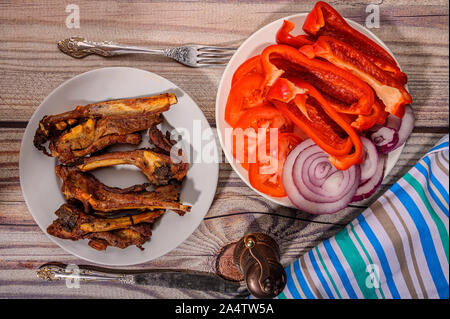 Côtes d'agneau mariné aux épices grillés dans un plat sur la table. Avec des tranches de tomates, poivrons et oignons Banque D'Images
