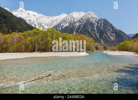 Les eaux claires de la Rivière Azusa fonctionnant par les arbres à Kamikochi avec le Japon les Alpes du Nord à l'arrière-plan. Banque D'Images