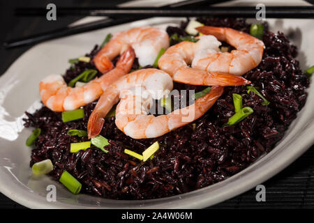 Riz noir cuit avec les crevettes et les oignons verts dans une assiette sur fond noir. Top View with copy space Banque D'Images