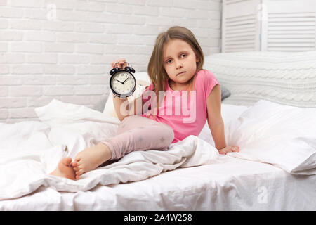 Fatigué sleepy petit enfant fille en pyjama avec réveil au lit. Bon matin Banque D'Images