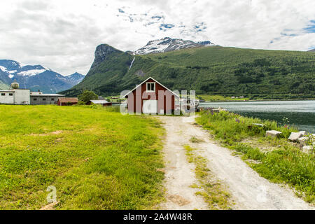 Maison en bois rouge traditionnelle norvégienne avec une cascade au loin. Chute d'Steindalsfossen, la Norvège. Banque D'Images