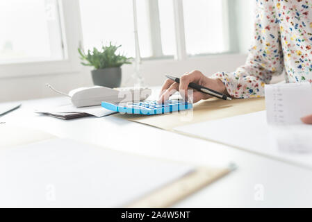 Businesswoman doing a calcul sur une calculatrice de bureau manuel, près de sa main tenant un stylo. Banque D'Images
