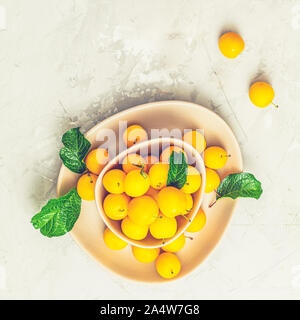 Modèle d'été créatif à base de produits frais dans les prunes cerises jaunes bol rose sur fond de béton gris. Concept minimal de fruits. Mise à plat. Banque D'Images