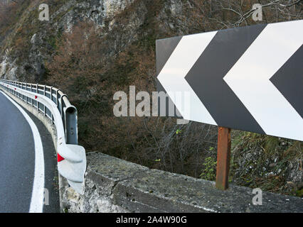 Un virage à gauche panneau de flèche de l'avant indique un virage dans une route de montagne Banque D'Images