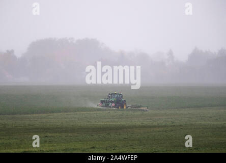 16 octobre 2019, le Brandebourg, Bernau/Ot Birkholz : Un agriculteur durs dans une pluie battante avec une faucheuse attelée au tracteur sur le terrain dans le district de Barnim. Photo : Soeren Stache/dpa-Zentralbild/ZB Banque D'Images