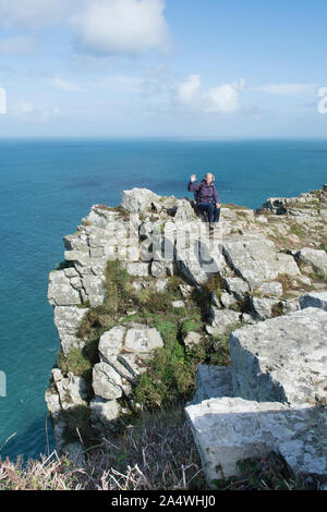 Femme assise sur un haut walker barre rocheuse au-dessus de la mer dans la Vallée des Roches, Lynton, Devon. Banque D'Images