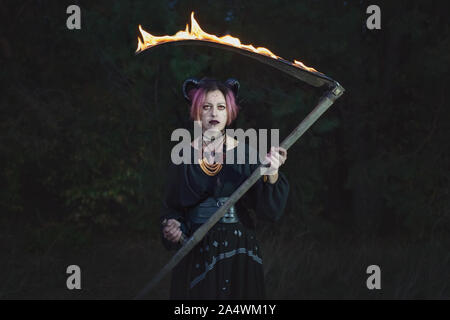 Grim Reaper féminin se tient dans le noir avec une faux. Banque D'Images