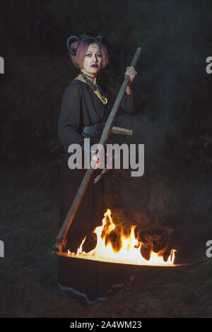 Femelle Grim Reaper tond l'herbe dans l'obscurité avec une faux. Banque D'Images