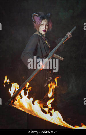 Sombre démon femelle tond l'herbe dans l'obscurité avec une faux. Banque D'Images