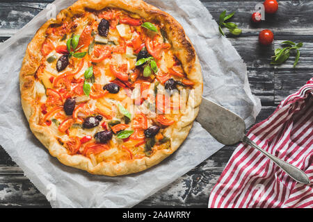 Des pizzas aux légumes sur un fond sombre. La pizza est vue de dessus et de l'est sur une plaque blanche, avec une serviette rouge et blanc next t Banque D'Images