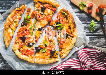 Des pizzas aux légumes sur un fond sombre. La pizza est coupée en morceaux de taille irrégulière, est vu de dessus. Avec un napk rouge et blanc Banque D'Images