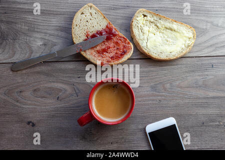 Une tranche de pain blanc, de confiture sur propagation il vus du dessus et une tasse à café rouge sur une table en bois Banque D'Images