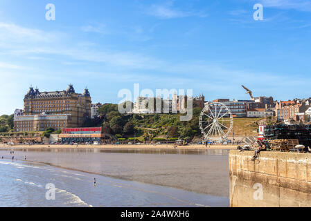 Les gens profiter du soleil sur la plage de Scarborough, à la fin de l'été. Un hôtel se trouve près de la plage comme une pointe s'étend vers la mer. Banque D'Images