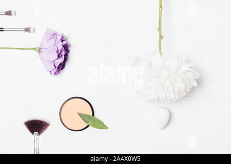 Produits de maquillage et accessoires de beauté télévision jeter l'arrière-plan. Poudre cosmétique, brosses et d'éponges près de fleurs fraîches sur tableau blanc, vue du dessus. Banque D'Images