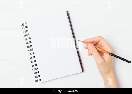 L'écriture main de femme en blanc modèle portable holding crayon sur table en bois blanc, vue du dessus. Banque D'Images