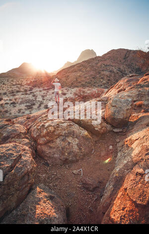Jeune homme tenant son chapeau tout en regardant à Spitzkoppe en Namibie - debout Banque D'Images