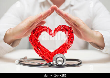 Coeur rouge avec stéthoscope protégés par les mains de l'homme. Santé et médecine concept. Assurance santé concept. Banque D'Images