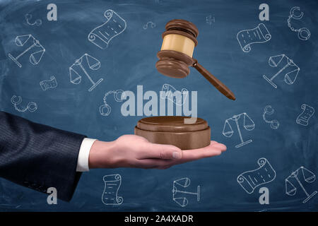 Un businessman's hand holding a sound block paume vers le haut et d'un maillet en bois planant au-dessus de lui. Banque D'Images