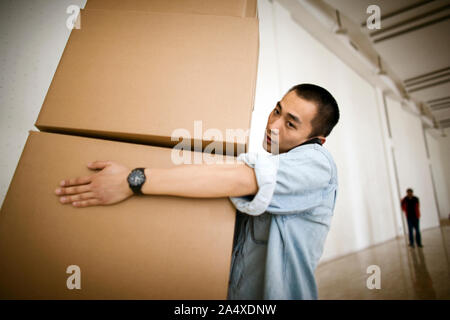 Young adult man carrying boxes et l'utilisation d'un cellulaire dans un bâtiment. Banque D'Images