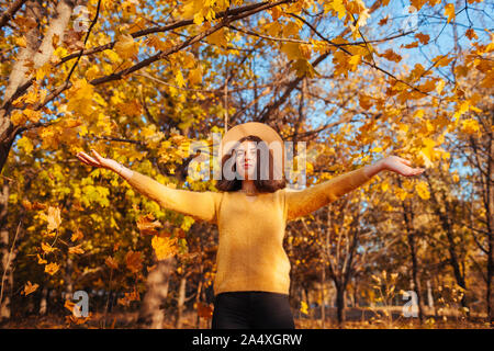 Activités de saison d'automne. Woman throwing leaves in autumn forest au coucher du soleil. Jeune femme ayant l'amusement à l'extérieur portant des vêtements élégants Banque D'Images