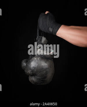 Le bras de l'homme enveloppé dans un bandage élastique noir sports détient old vintage paire de gants de boxe en cuir, fond noir Banque D'Images