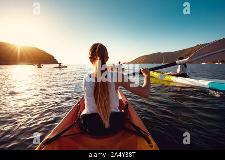 Grand groupe de kayaks avec des amis est la marche dans la baie de la mer au coucher du soleil Banque D'Images