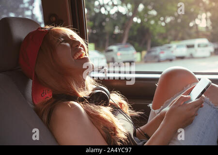 Young Asian girl laughing millénaire lors de l'utilisation de messagerie sur son smartphone à l'intérieur d'une voiture - bonne femme divers dans le véhicule des messages sur téléphone mobile Banque D'Images