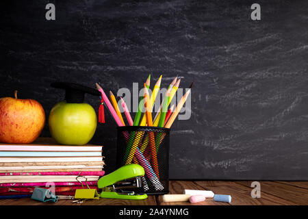 L'éducation ou Concept retour à l'école. Fournitures scolaires colorés avec des livres, crayons de couleur, calculatrice, stylo cutter clips et pomme verte on chalkboard ba Banque D'Images